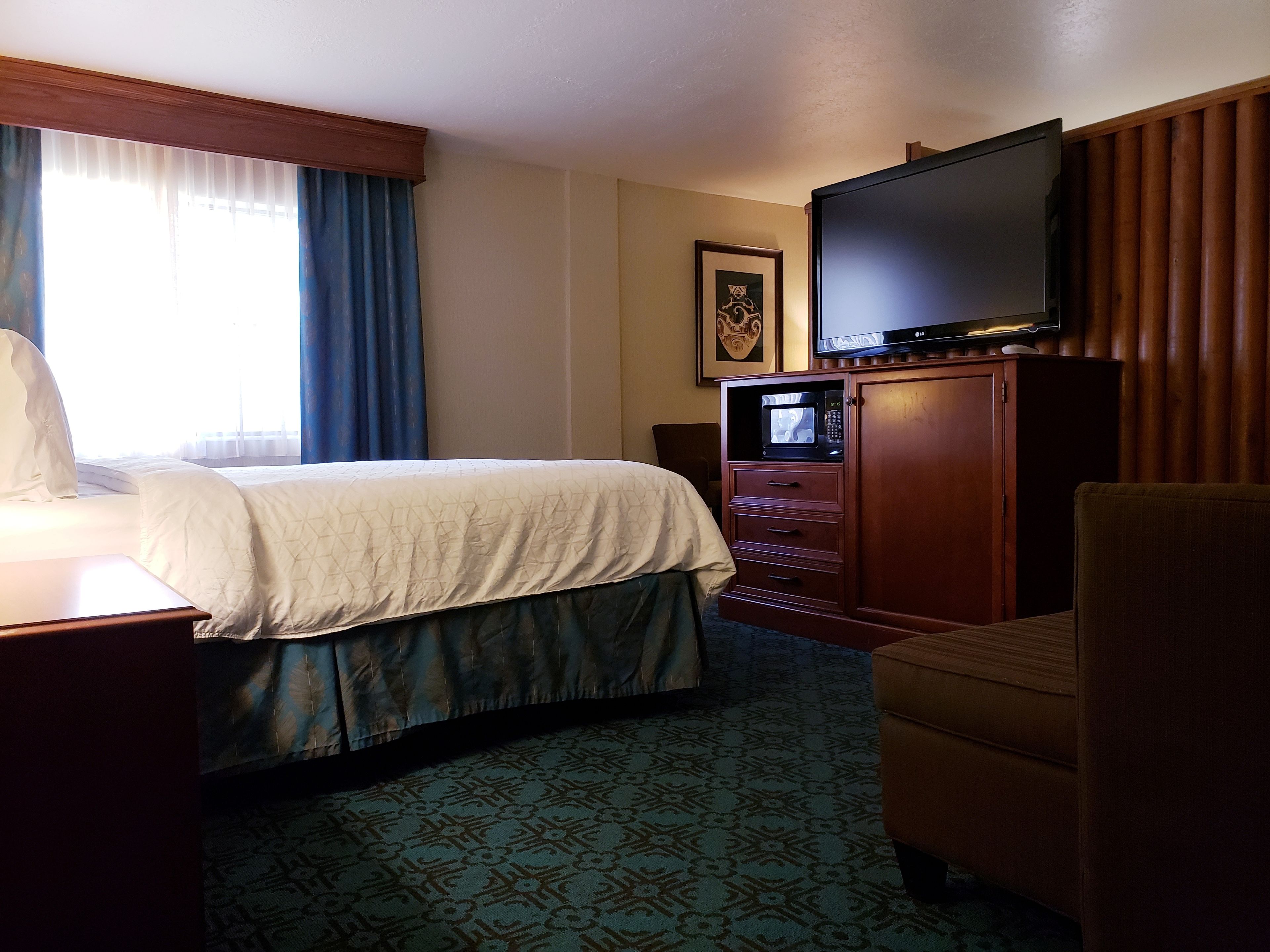 A hotel room with a bed, a television on a wooden cabinet, a chair, and a patterned carpet.