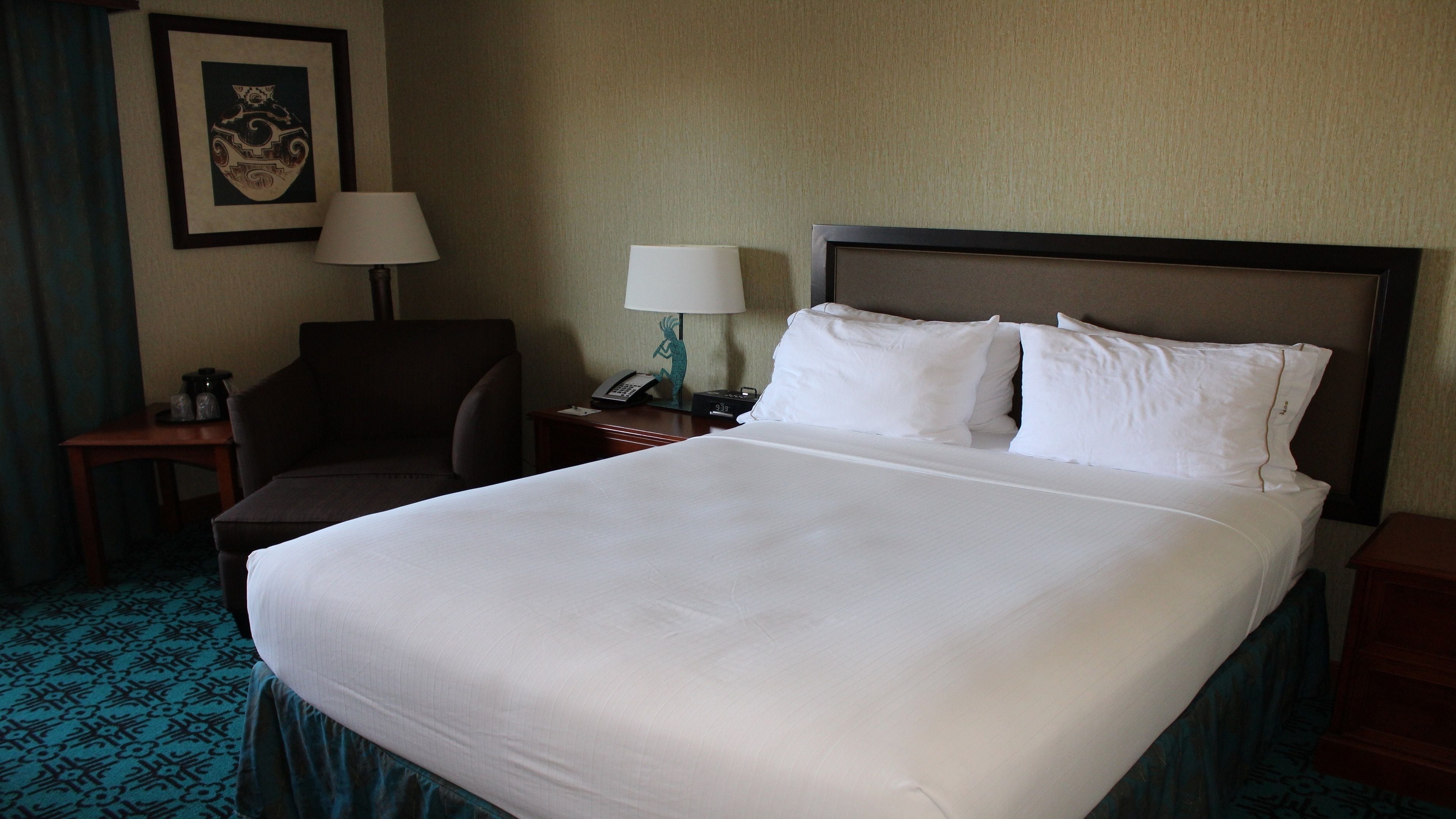 A hotel room with a large bed, two bedside lamps, a chair, a small table, and a wall-mounted telephone.