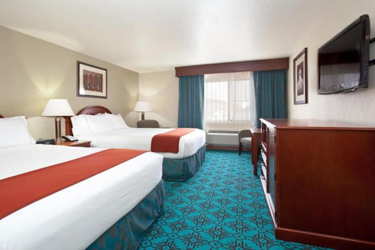 A hotel room with two beds, a desk, a TV, and a window with curtains.