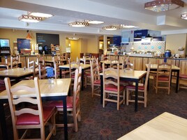 Un restaurante con varias mesas y sillas de madera, una barra de café y una sección de pastelería.