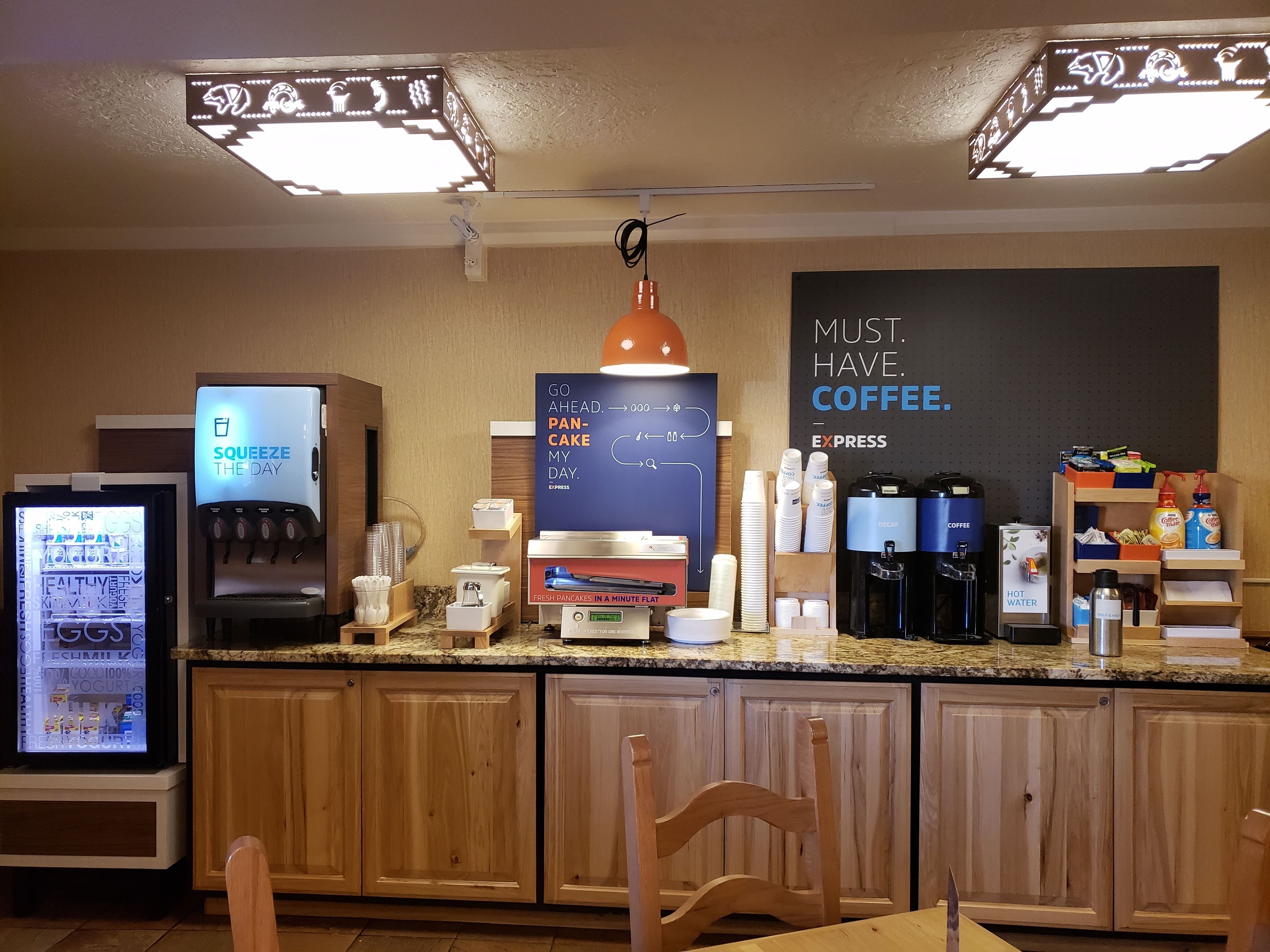 Un comptoir de petit-déjeuner équipé d’une machine à café, d’un réfrigérateur rempli de produits frais et d’un panneau indiquant : « UN CAFÉ, C’EST INDISPENSABLE ».