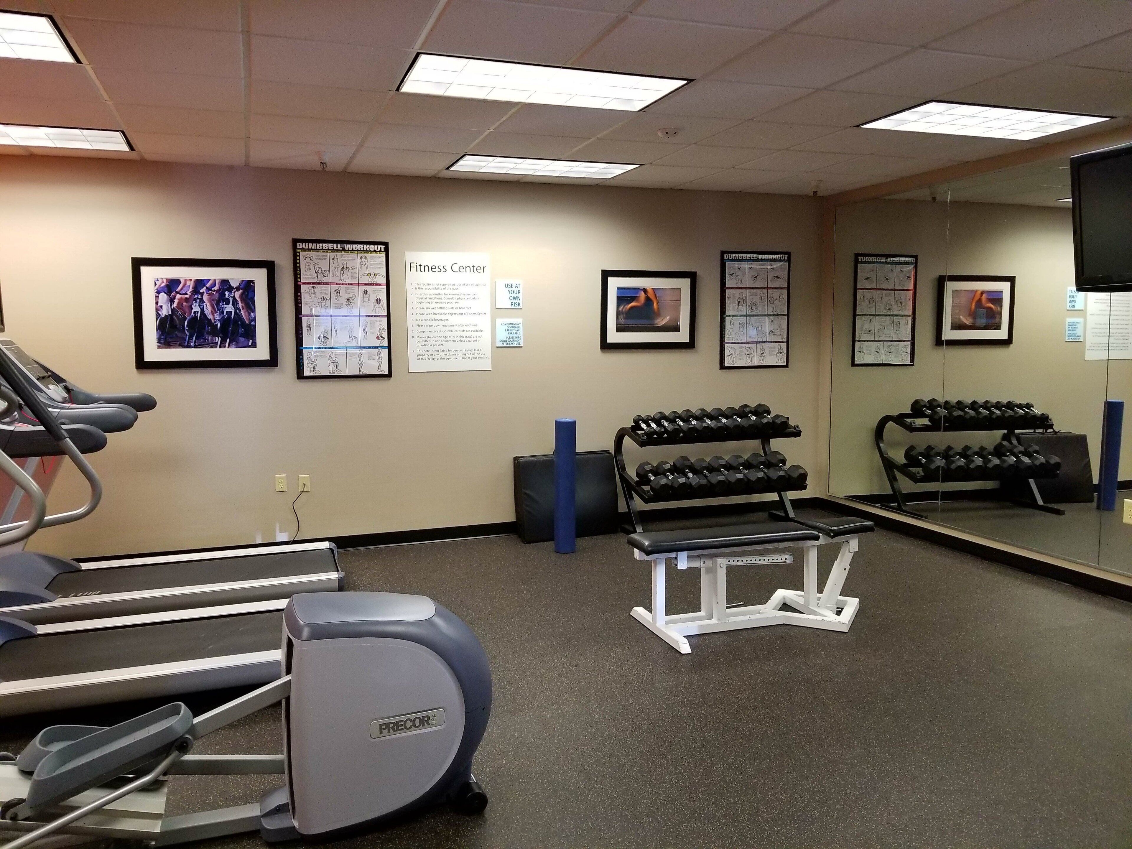 A fitness center with treadmills, dumbbells, and exercise posters on the walls.