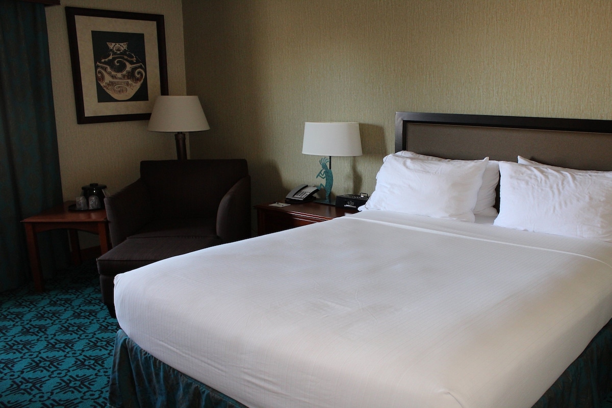 A hotel room with a large bed, two bedside lamps, a chair, a nightstand, and a framed picture on the wall.