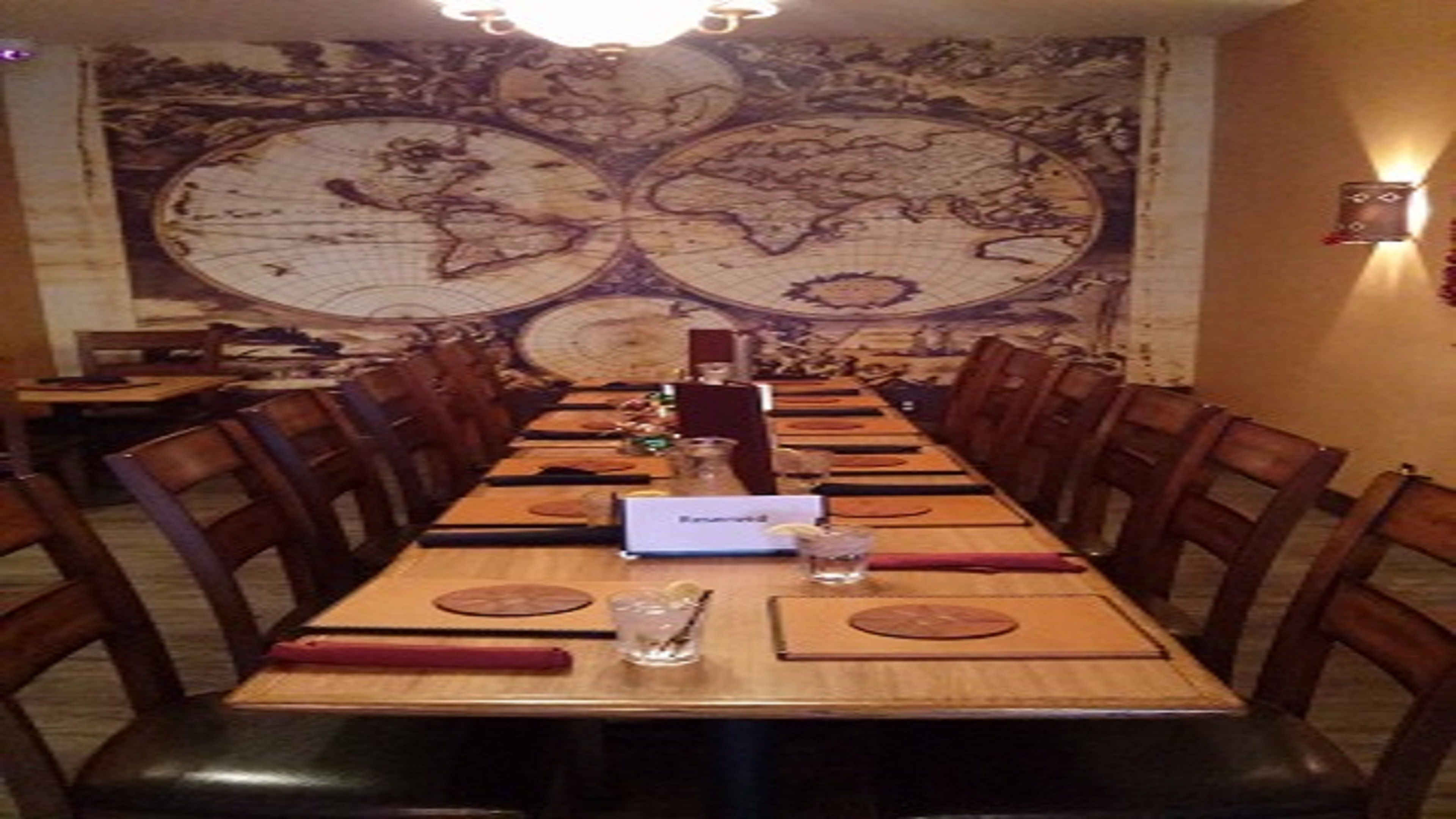 A long dining table with chairs, a world map on the wall, and a menu stand.