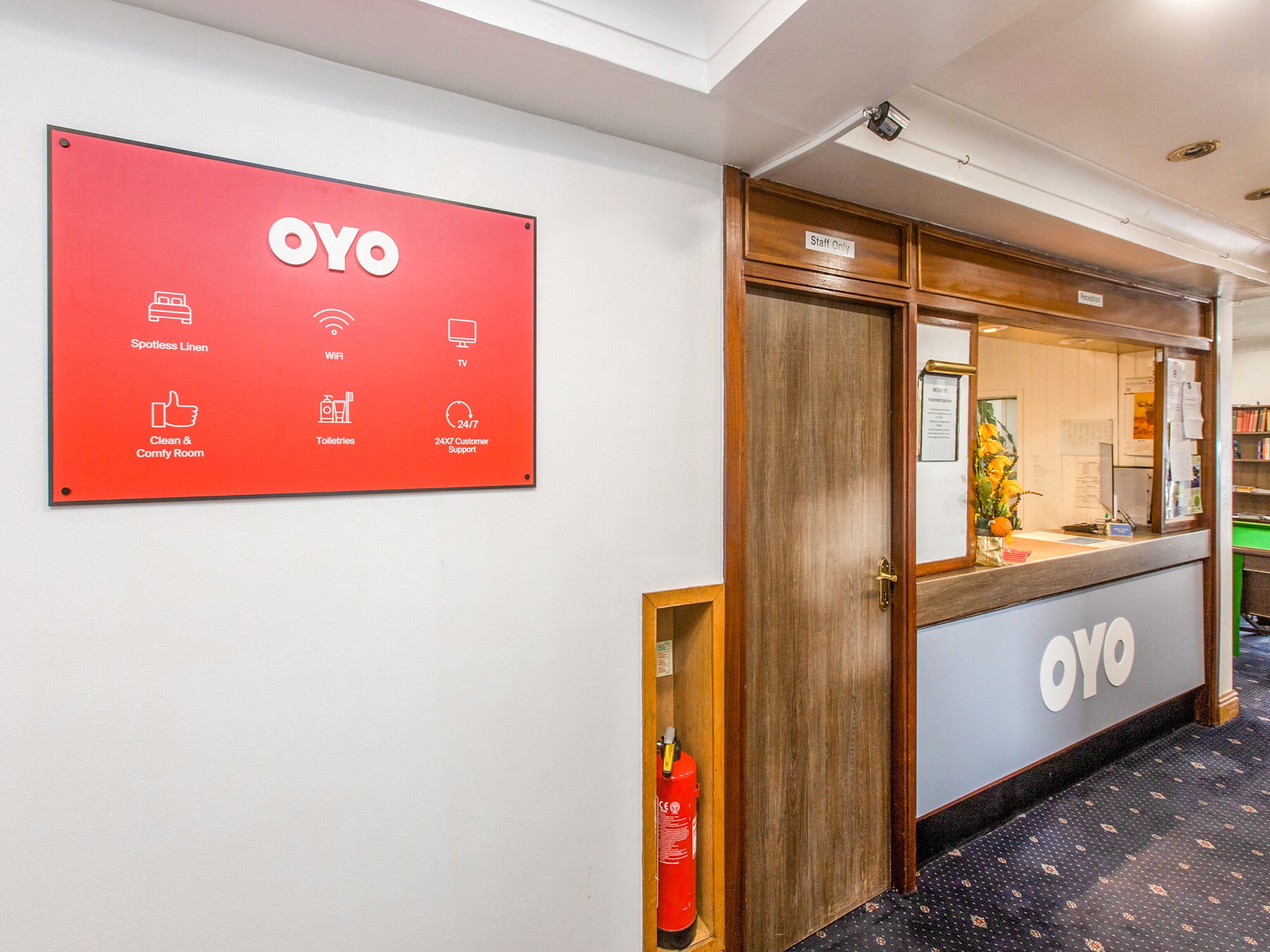 En hotellreception med en skylt som listar bekvämligheter som fläckfritt sänglinne, Wi-Fi, TV, toaletter och kundsupport dygnet runt.