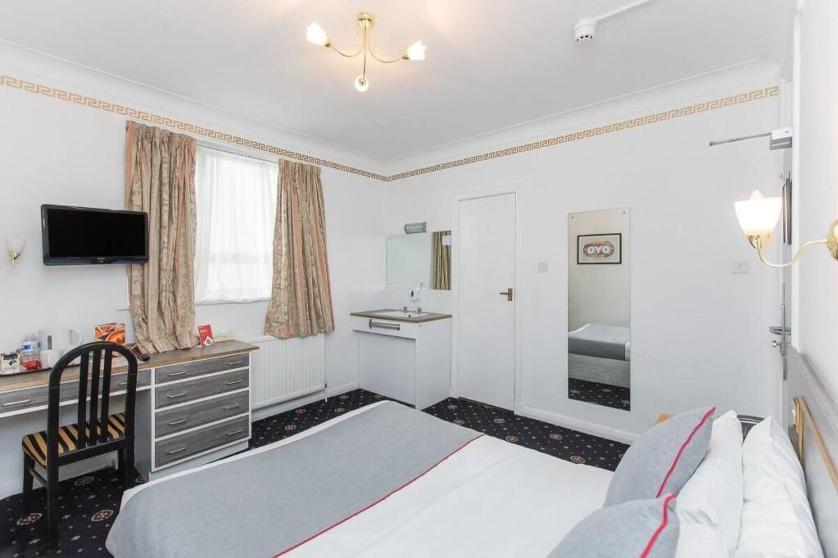 Habitación de hotel con cama, escritorio con silla, televisor, espejo y ventana con cortinas.