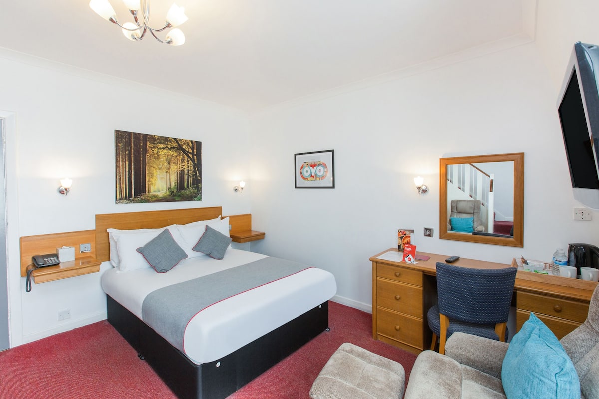 Habitación de hotel con cama, mesitas de noche, escritorio, silla, espejo y un cuadro en la pared.