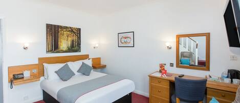 Habitación de hotel con cama, mesitas de noche, escritorio, silla, espejo y un cuadro en la pared.
