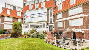 A hotel with a sign reading "OYO Stade Court Hotel," featuring a brick facade, a well-maintained lawn, and outdoor seating area. - OYO Stade Court Hotel (Hythe)