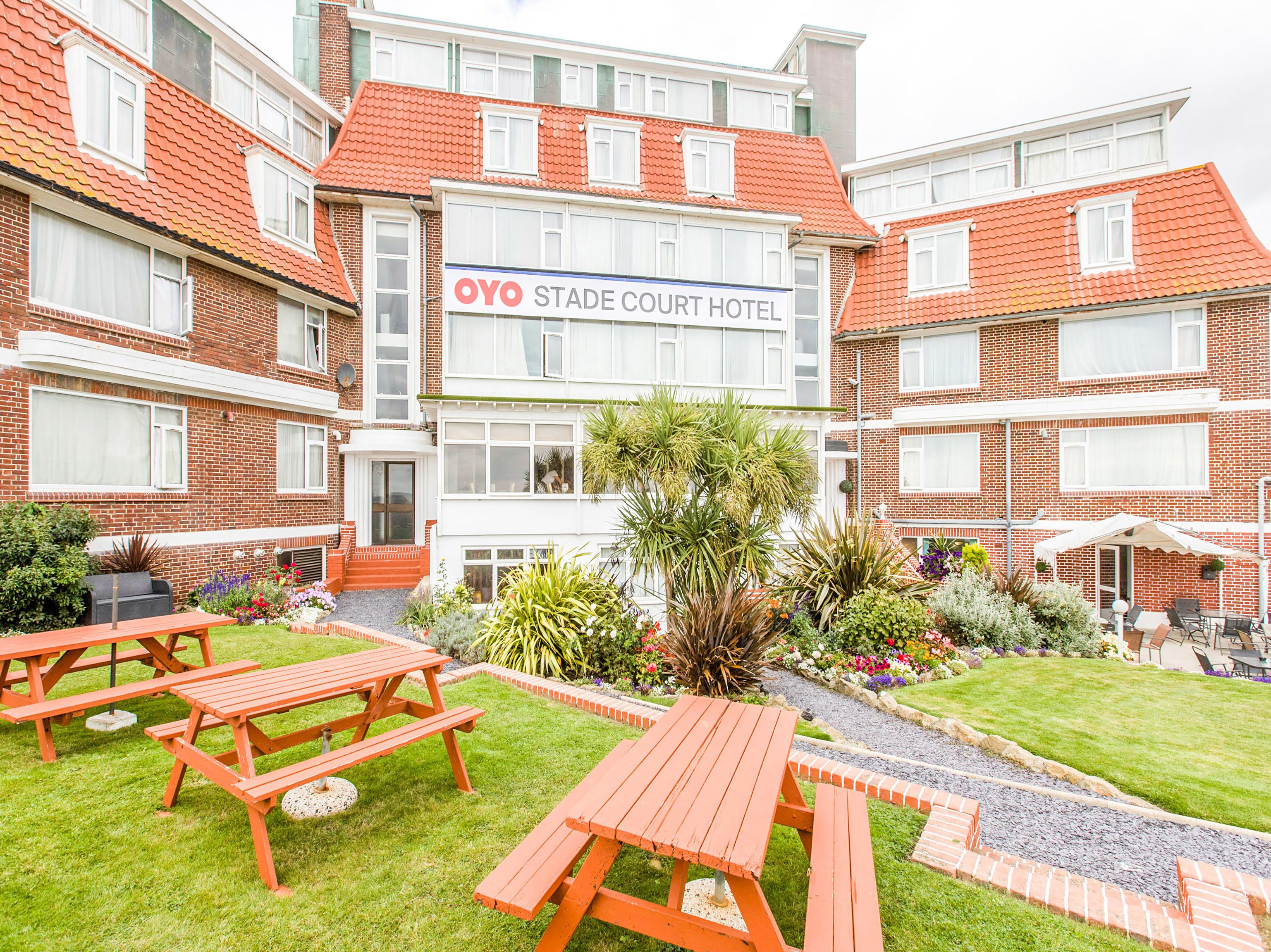 Un hotel con un letrero que dice "OYO STADE COURT HOTEL". Hay mesas de picnic en el jardín.