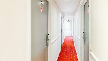 Un couloir avec un tapis rouge à motifs, des murs blancs et des portes ornées de panneaux « interdiction de fumer ».