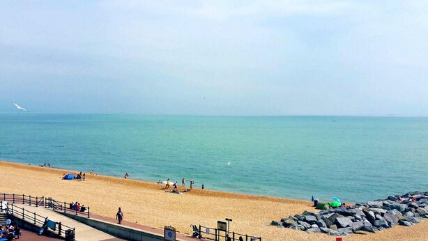 A beach with people sunbathing and swimming, a rocky breakwater, and a clear sky. - OYO Stade Court Hotel (Hythe)