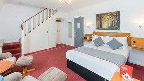 A hotel room with a bed, a desk, a chair, a staircase, and a painting on the wall. - OYO Stade Court Hotel (Hythe)