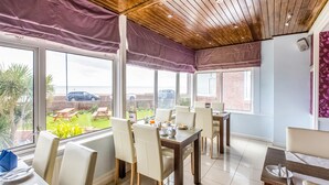 A dining area with a view of the sea, wooden ceiling, and large windows. - OYO Stade Court Hotel (Hythe)
