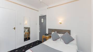 A hotel room with a bed, bedside table, lamp, and a mirror.