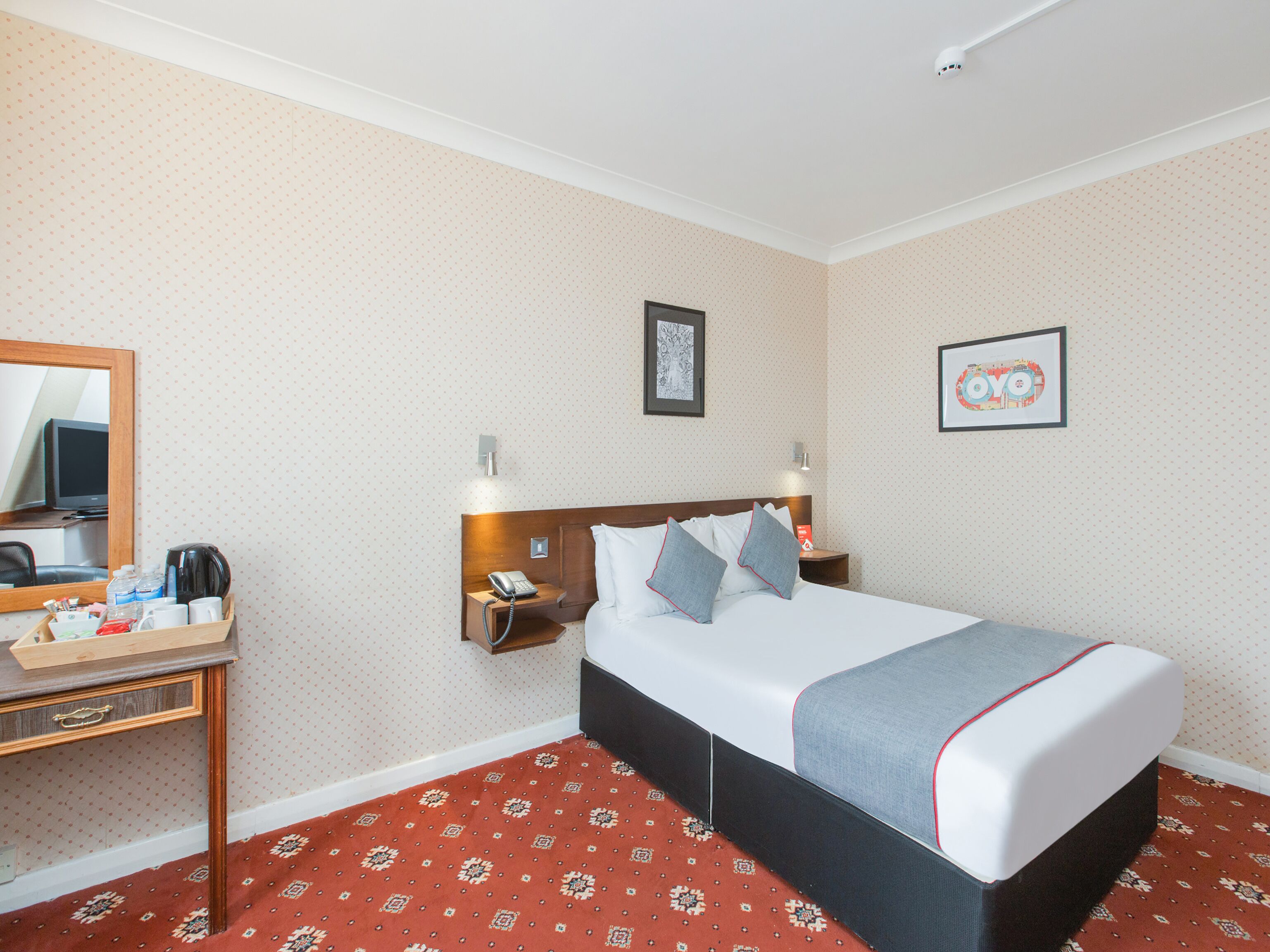 Une chambre d’hôtel comprenant un lit, des tables de chevet, un miroir, un téléphone fixé au mur et un tableau encadré.