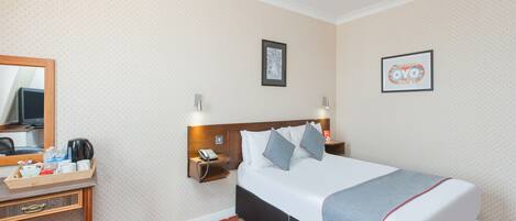A hotel room with a bed, bedside tables, a mirror, a wall-mounted telephone, and a framed picture.