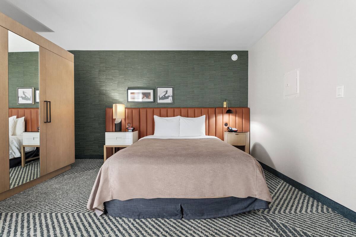 Habitación de hotel con cama, mesitas de noche, un espejo y una pared verde decorativa.