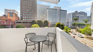 Een balkon met een tafel en stoelen, met uitzicht op een stadsgezicht met verschillende gebouwen en een straat met auto's.