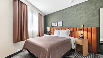 A hotel room with a large bed, a wooden headboard, a nightstand with a lamp, and a view of the outdoors through the window.