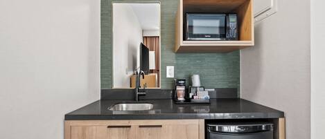 A modern kitchen with a black countertop, wooden cabinets, a built-in microwave shelf, and a dishwasher.