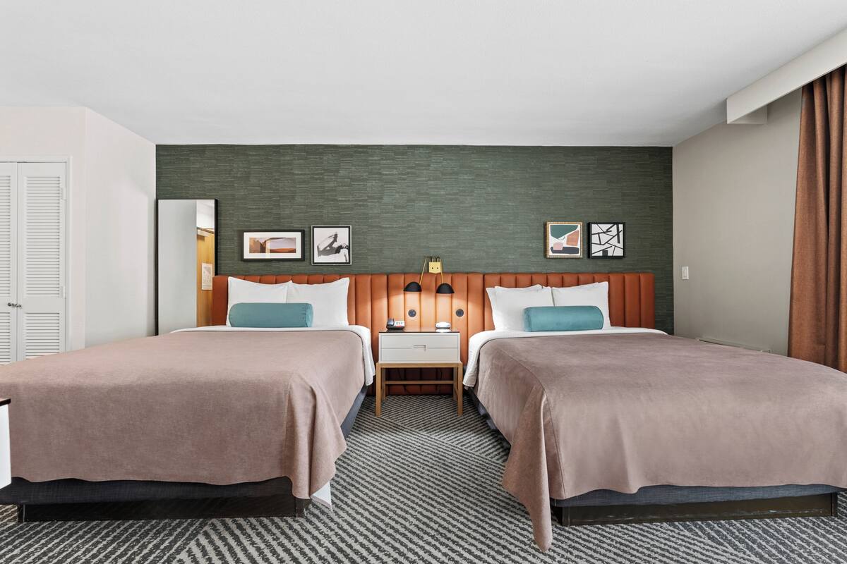 Een hotelkamer met twee bedden, een nachtkastje en een groene accentmuur.