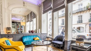 Une pièce avec un canapé bleu, un fauteuil jaune, une table basse ronde et une vue sur la rue.