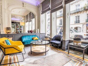 Ein Zimmer mit einem blauen Sofa, einem gelben Sessel, einem runden Couchtisch und Blick auf die Straße.