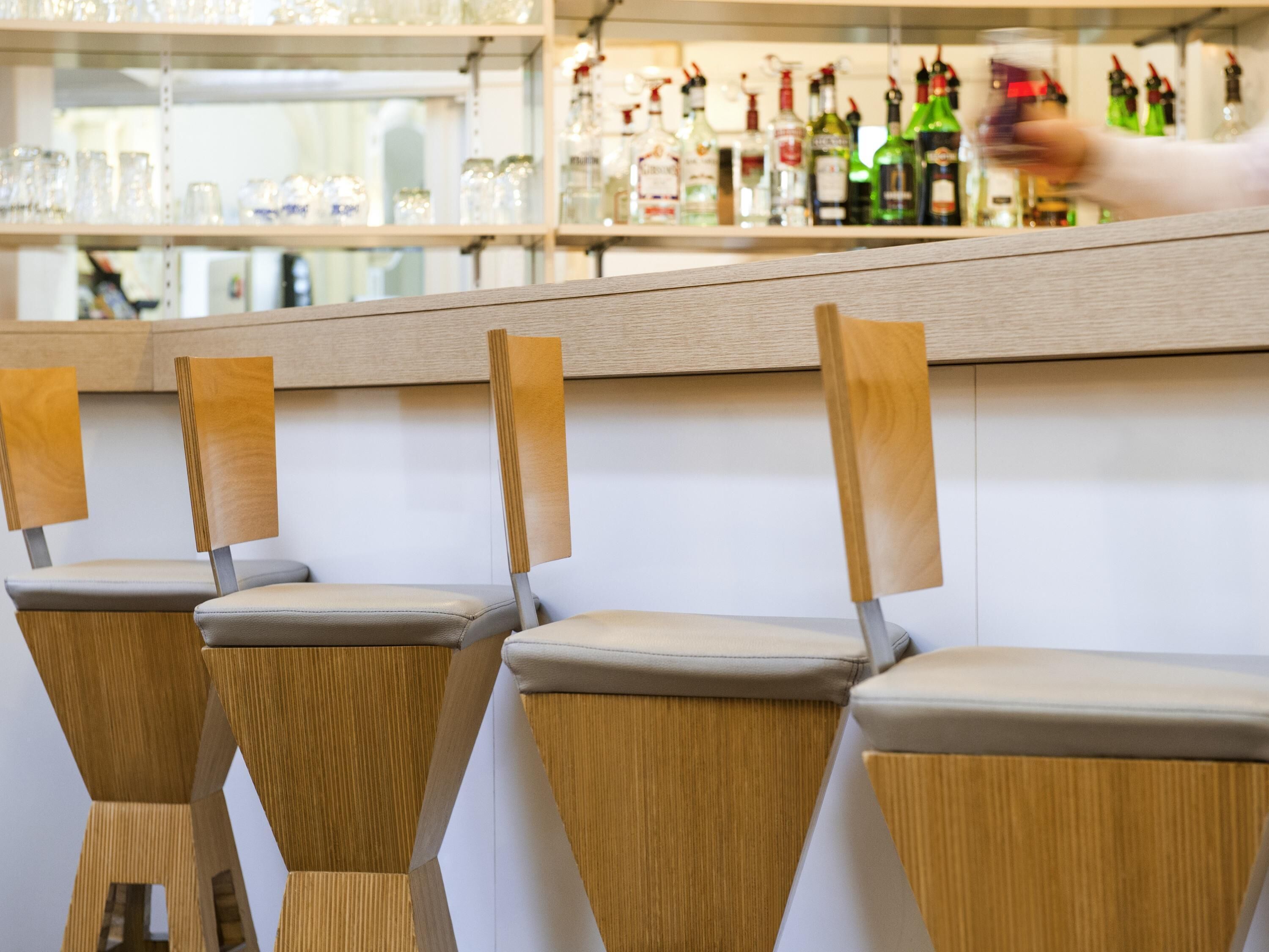 A bar area with wooden chairs and a counter displaying various bottles.