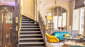 Un escalier menant à un hall d’entrée où se trouvent un canapé bleu, un fauteuil jaune et une petite table avec une lampe.