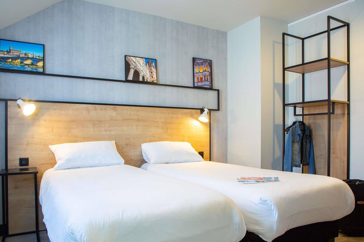 Un lit double avec du linge de lit blanc, une tête de lit en bois et deux lampes fixées au mur.