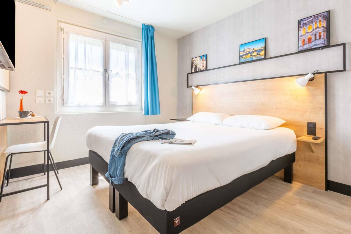 Une chambre d’hôtel moderne équipée d’un lit, d’une table de chevet, d’une chaise et d’une fenêtre avec des rideaux.