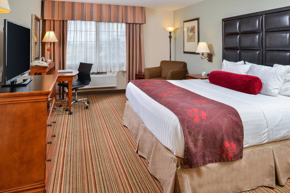 A hotel room with a large bed, a desk with a chair, a television, and a window with curtains.