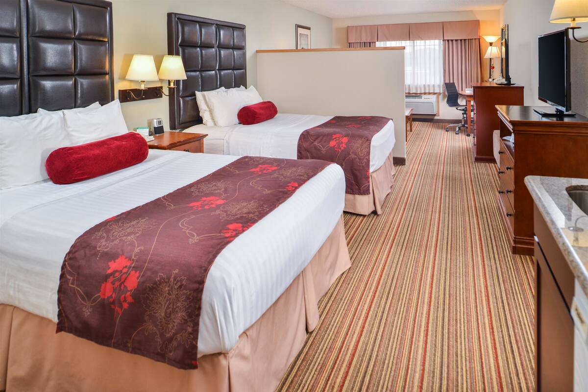 A hotel room with two beds, a desk, a television, and a bathroom.