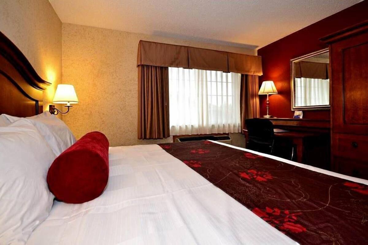 A hotel room with a large bed, a desk, a chair, and a mirror.