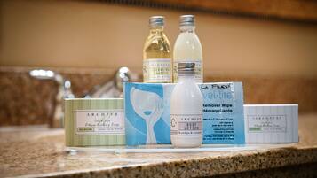A bathroom counter with various toiletries including bottles of liquid soap, a bar of body lotion, a bar of shea butter soap, and a packet of wipes.