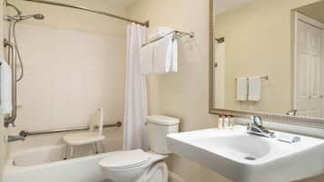 Un baño con bañera, inodoro y lavabo, equipado con una silla de ducha y barras de apoyo.