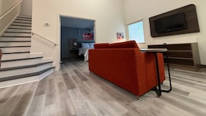 Un salon moderne avec un escalier, un canapé rouge, un téléviseur à écran plat et un plancher en bois.