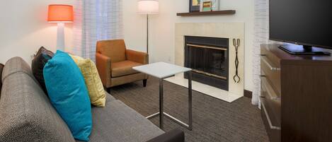 A modern living room with a sofa, armchair, small table, TV, fireplace, and lamps.