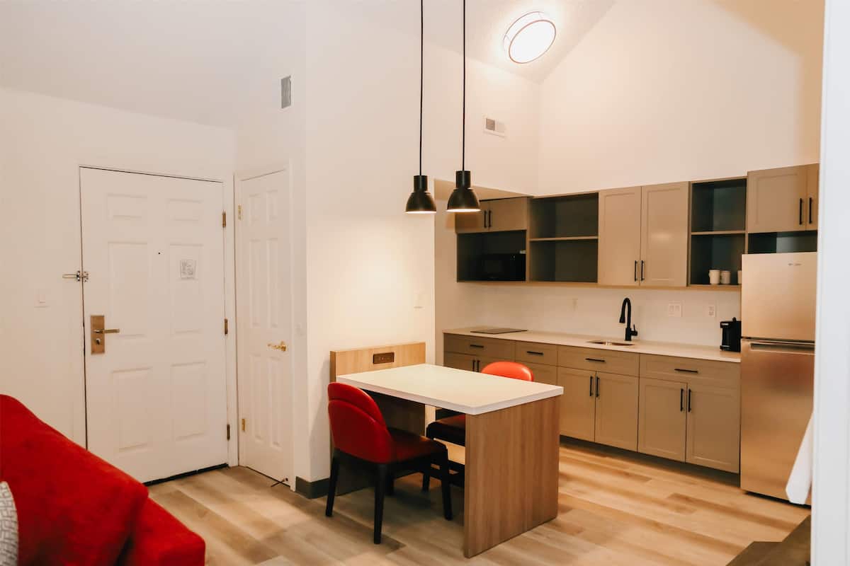 Una cocina compacta con una isla central, iluminación colgante y una silla roja.