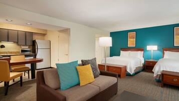 A hotel room with a kitchenette, two beds, a sofa, and a dining area.