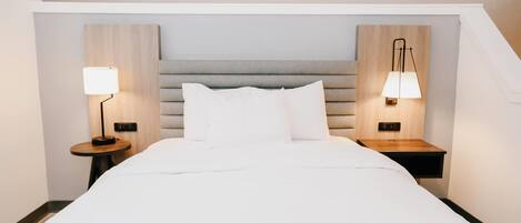 Una habitación de hotel con una cama grande, dos mesitas de noche con lámparas y un cabecero de madera.