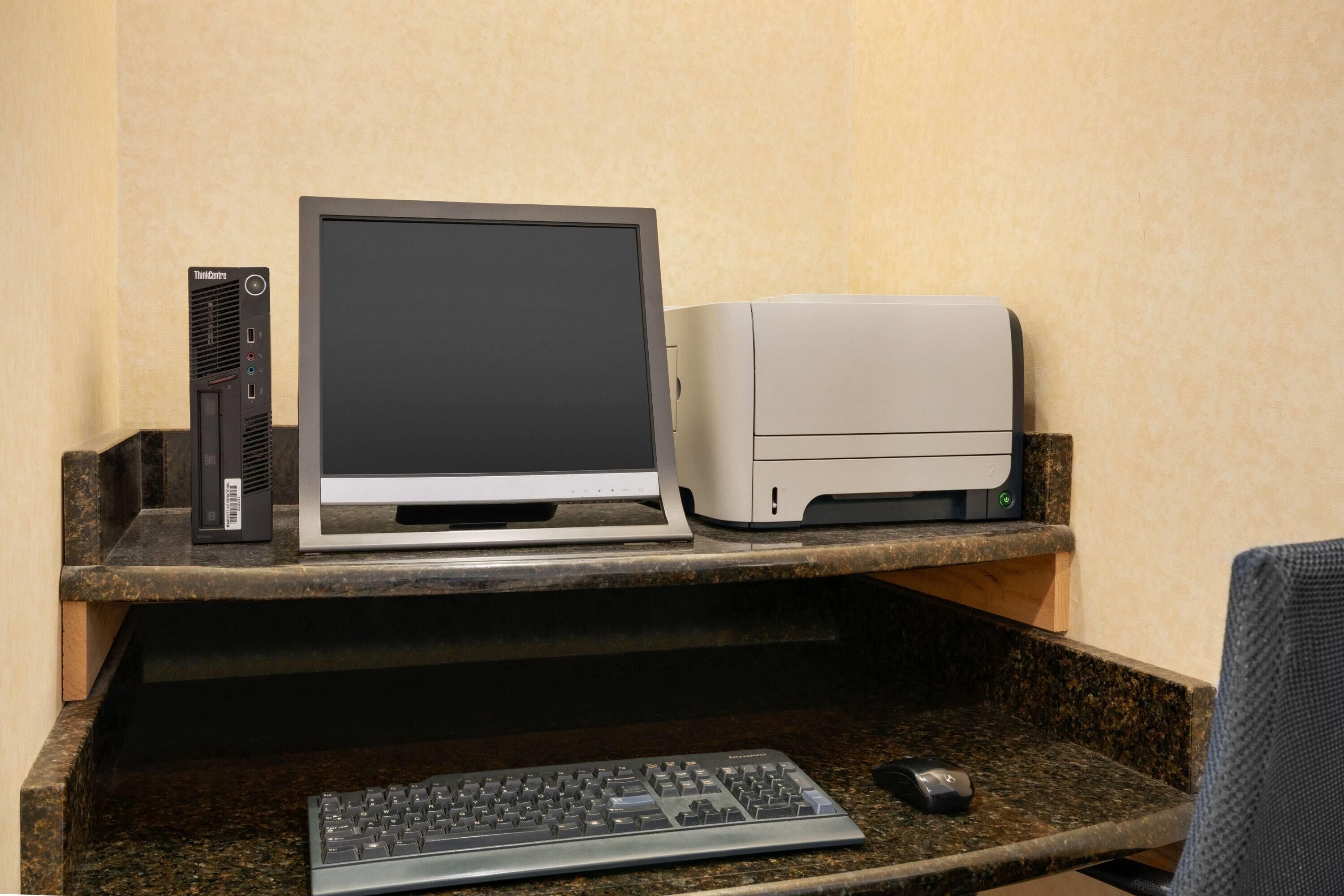 Un equipo de computadora de escritorio con monitor, impresora, teclado y ratón sobre una encimera de granito.