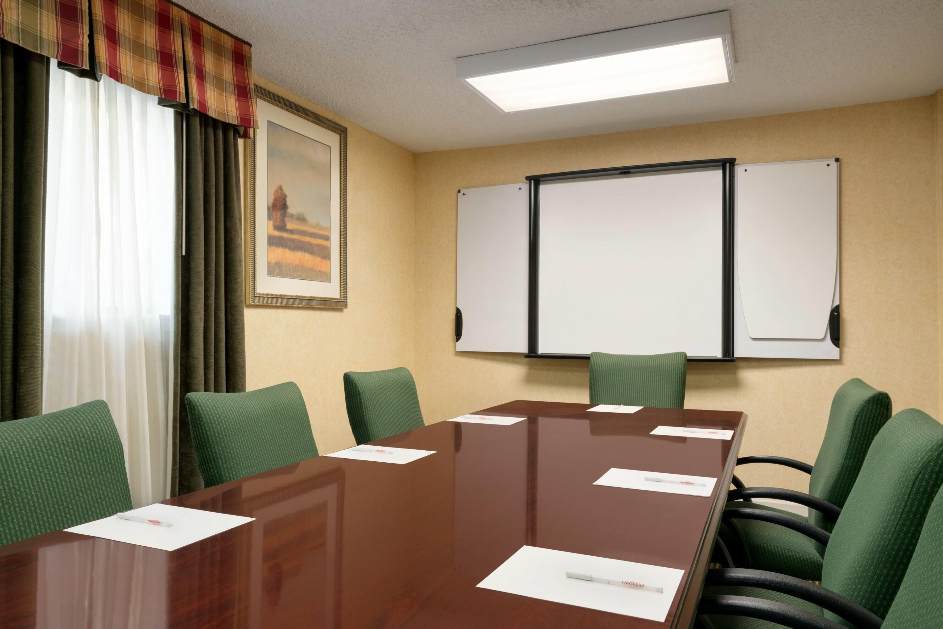 Un salón de conferencias con una mesa de madera, sillas tapizadas en verde, una pizarra y un cuadro en la pared.