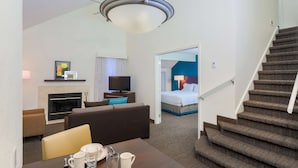 Une chambre d’hôtel comprenant un coin salon, une cheminée, une télévision, un lit et un escalier.