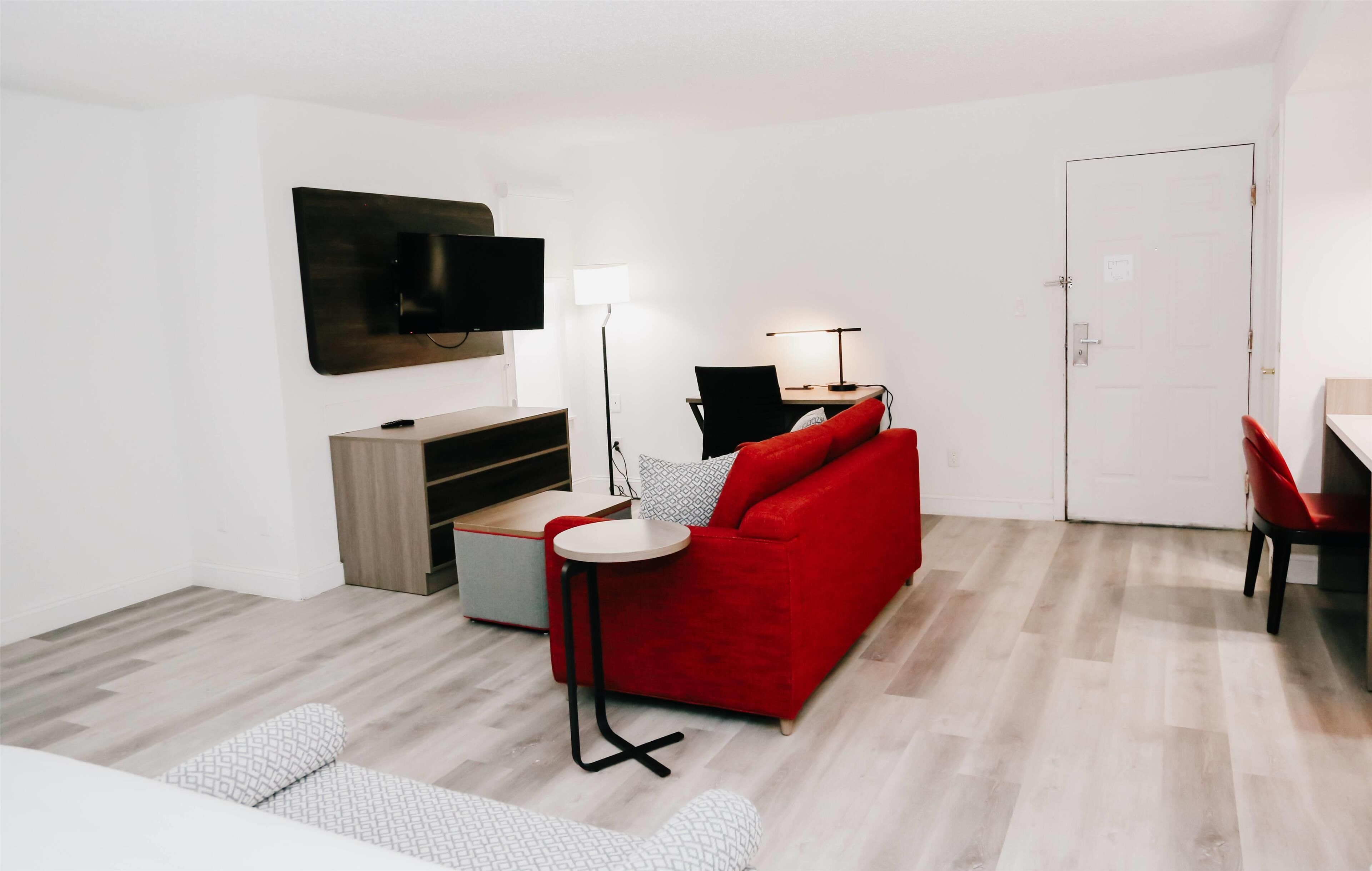 Un salon moderne avec un canapé rouge, une petite table ronde, un téléviseur fixé au mur et un bureau avec une chaise.