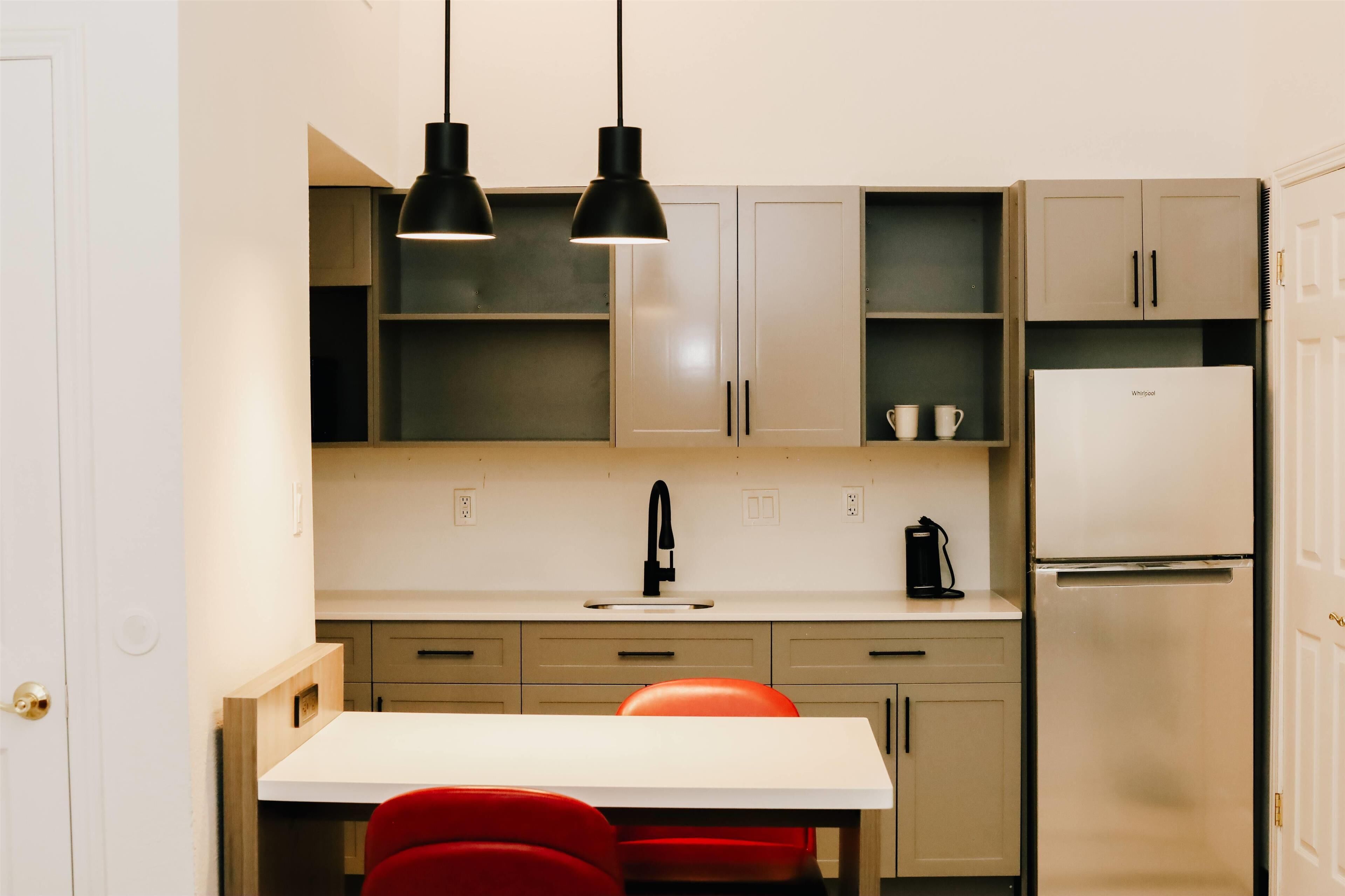 A compact kitchen with a white countertop, two pendant lights, a sink, and a built-in refrigerator.