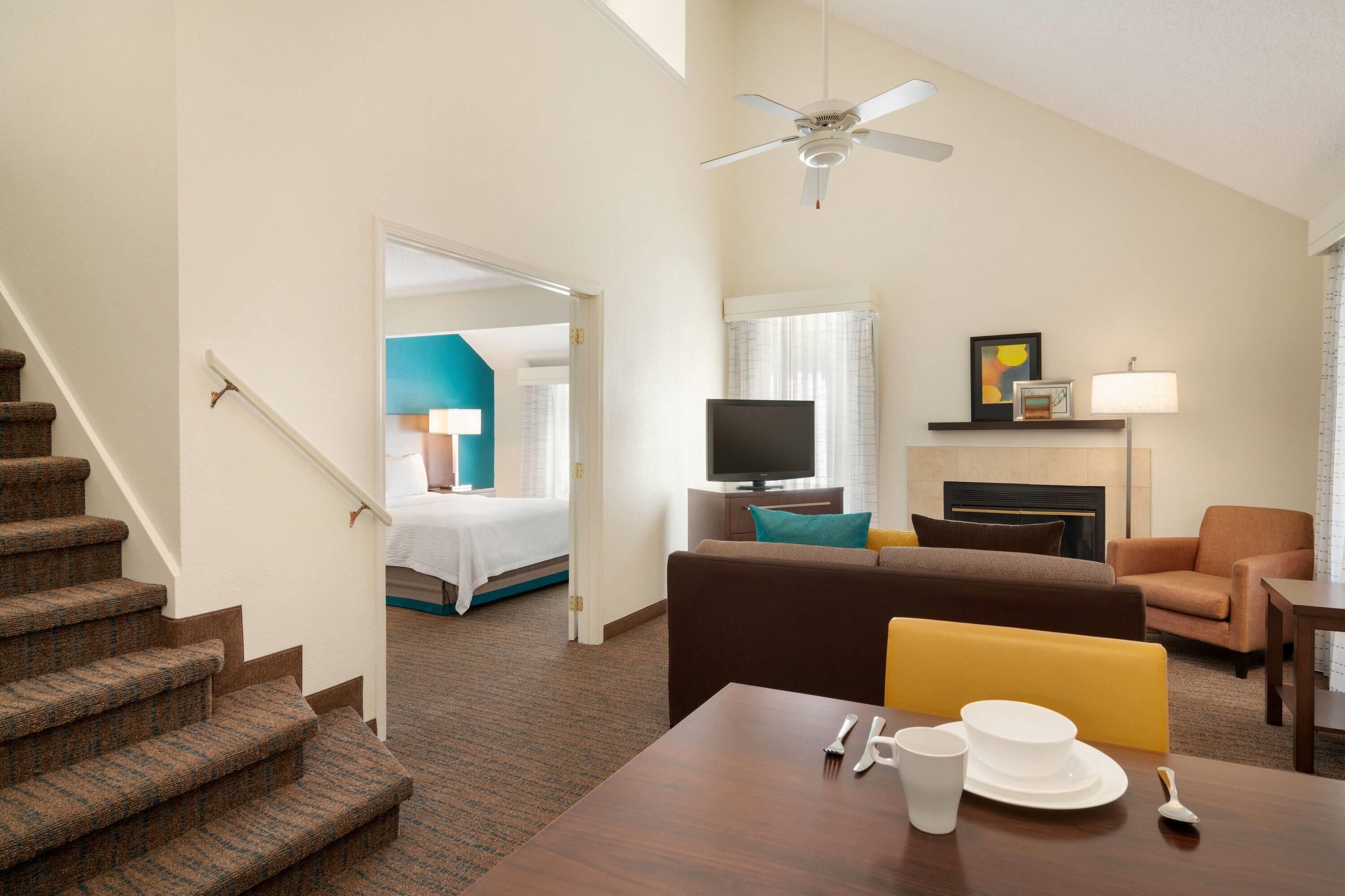 Habitación de hotel con una escalera, una sala de estar con sofá, una mesa de comedor, un televisor y una chimenea.