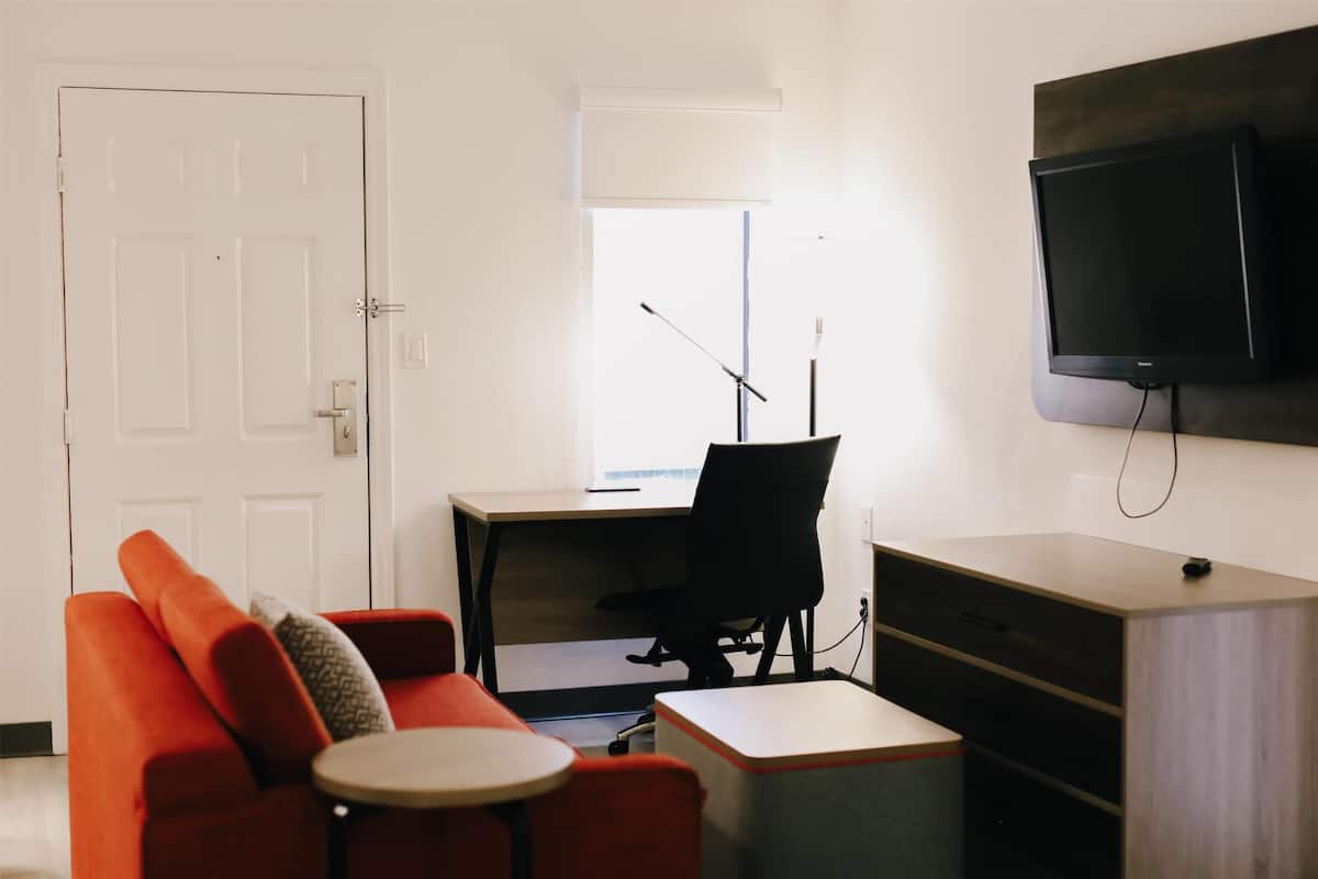 Una sala de estar moderna con un sofá, una mesita, un escritorio y un televisor montado en la pared.