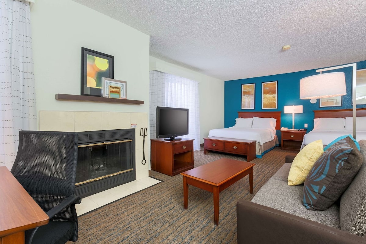 Una habitación de hotel con chimenea, televisión, cama, sofá y escritorio.